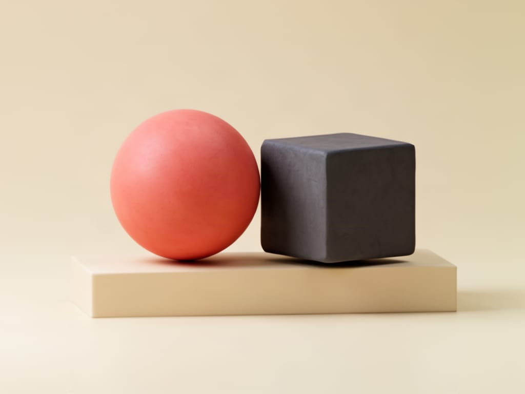 Abstract sculpture of a coral sphere and charcoal cube resting on a plinth